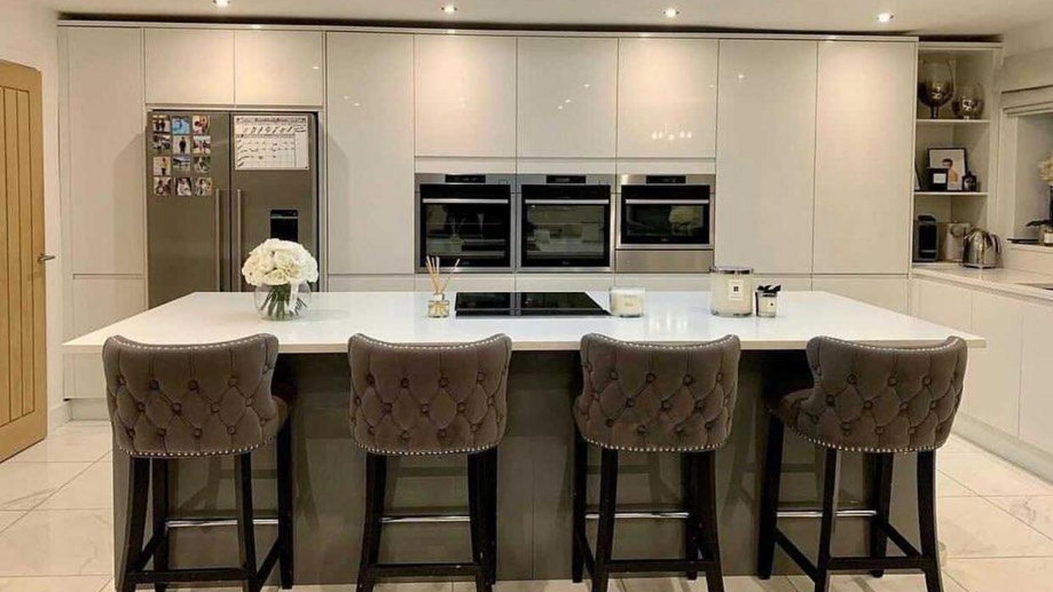 White gloss open-plan kitchen with an island, four grey stools and integrated appliances built into the wall.