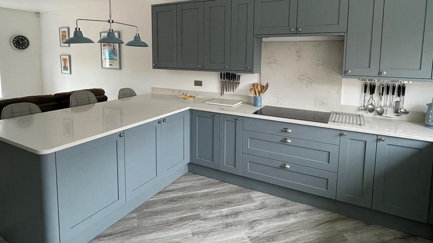Light blue open plan kitchen with shaker doors, silver cup handles, white worktops and a breakfast bar.