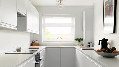 A white integrated handle kitchen makeover with white worktops and wooden floor.