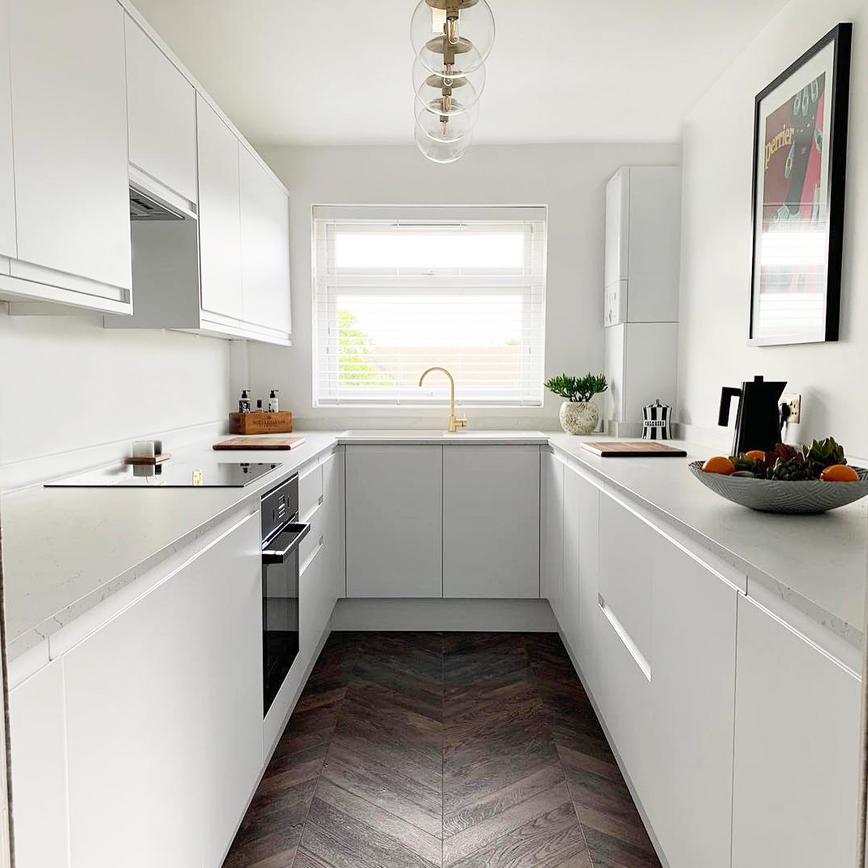 A white integrated handle kitchen makeover with white worktops and wooden floor.