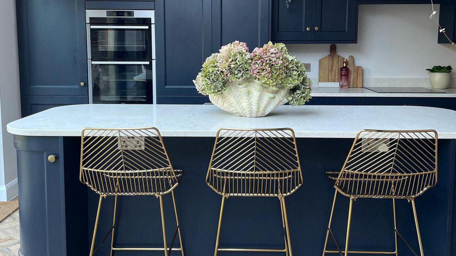 Charcoal shaker kitchen design with an island, quartz worktop, brass knob handles and flowers.