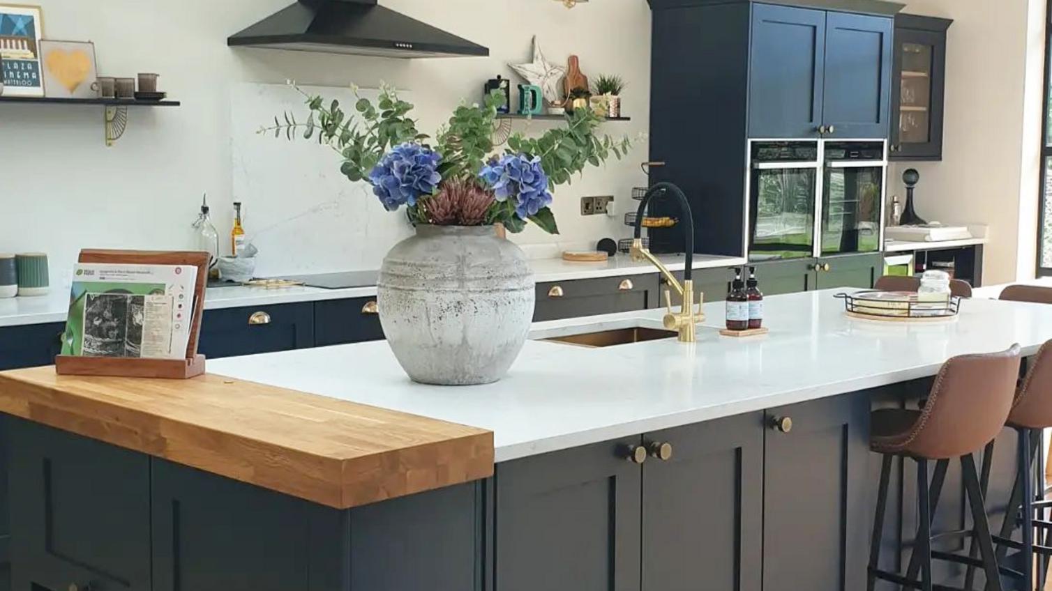 Navy shaker kitchen design with island, quartz and solid wood worktop, and brass cup and knob handles.