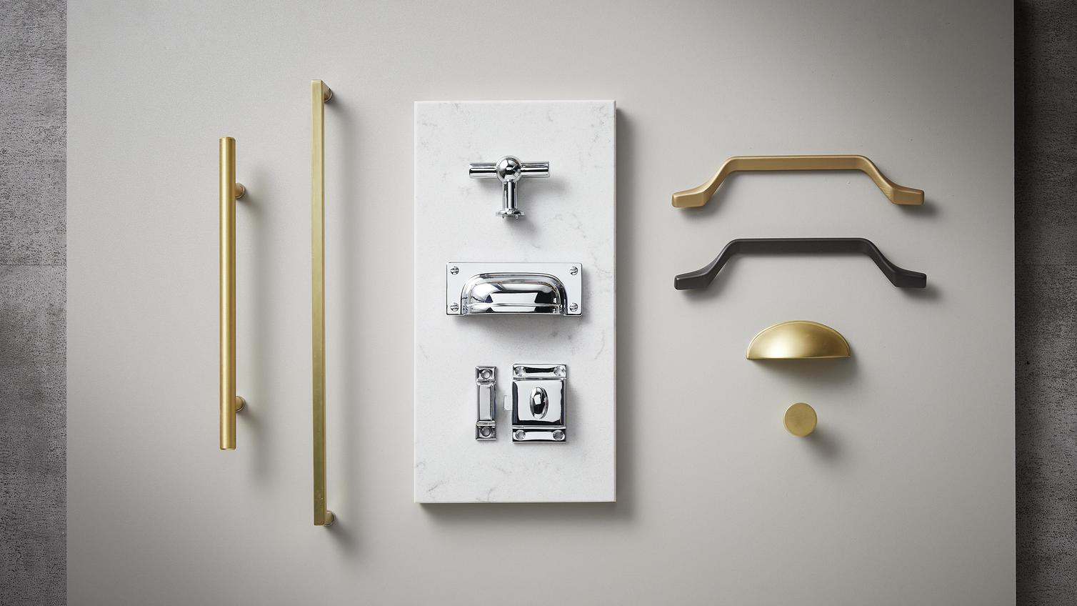 Elegance flat lay showing chrome bar handles, chrome hinges, and a black cabinet handle on a dove-grey background.