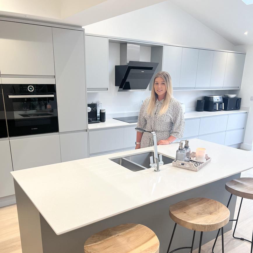 A calm haven kitchen makeover with grey integrated handle doors in an island layout. Has white worktops and a black oven.