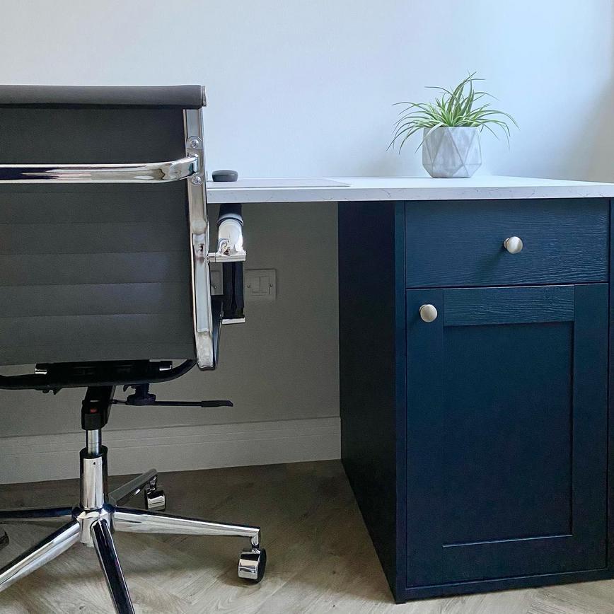 Home office design idea with navy shaker drawers, chrome knob handles, a white desk, and a black and silver office chair.