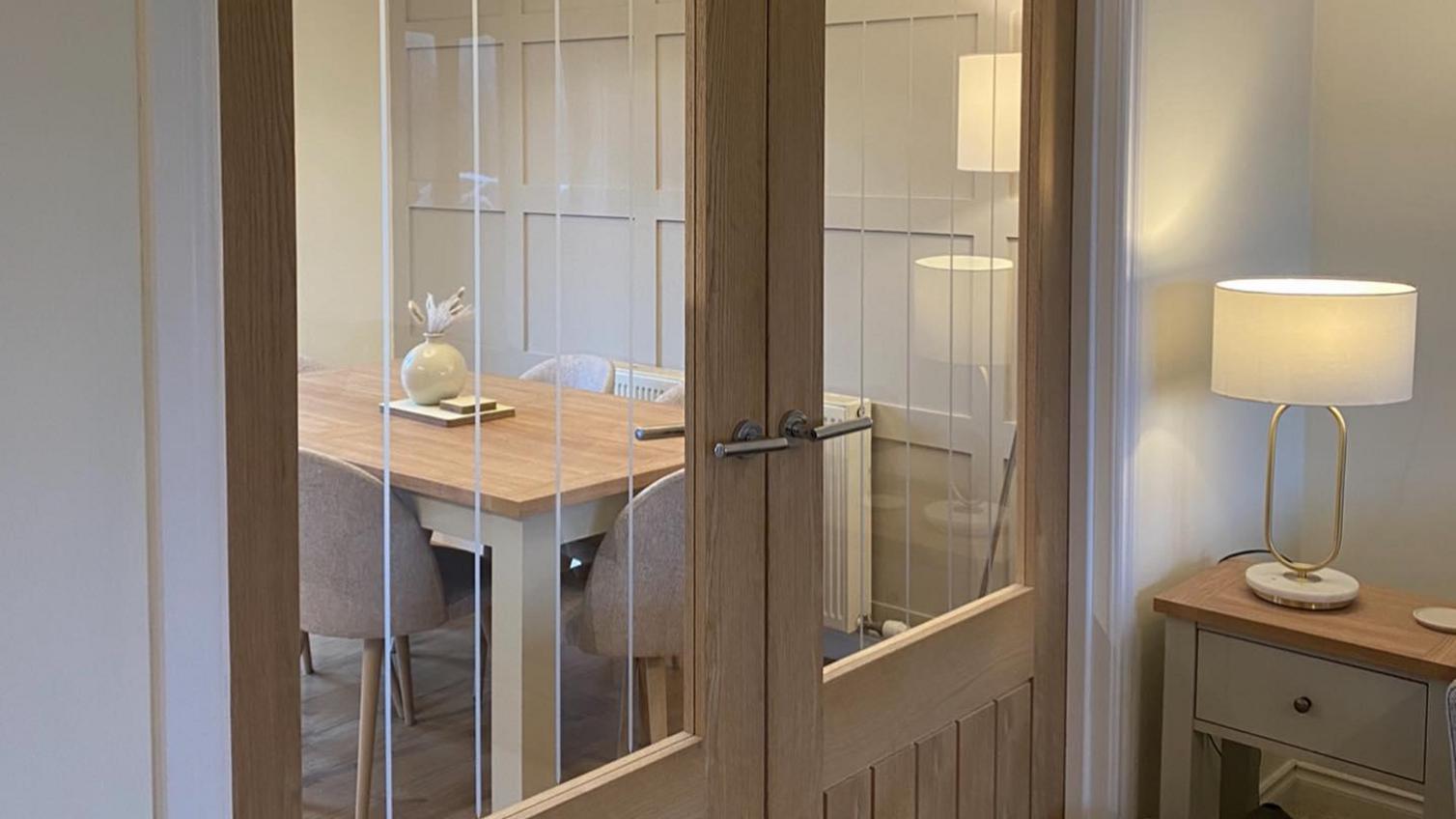 Light oak double internal doors with glass panels, showing a dining room with an oak table and grey walls and chairs.