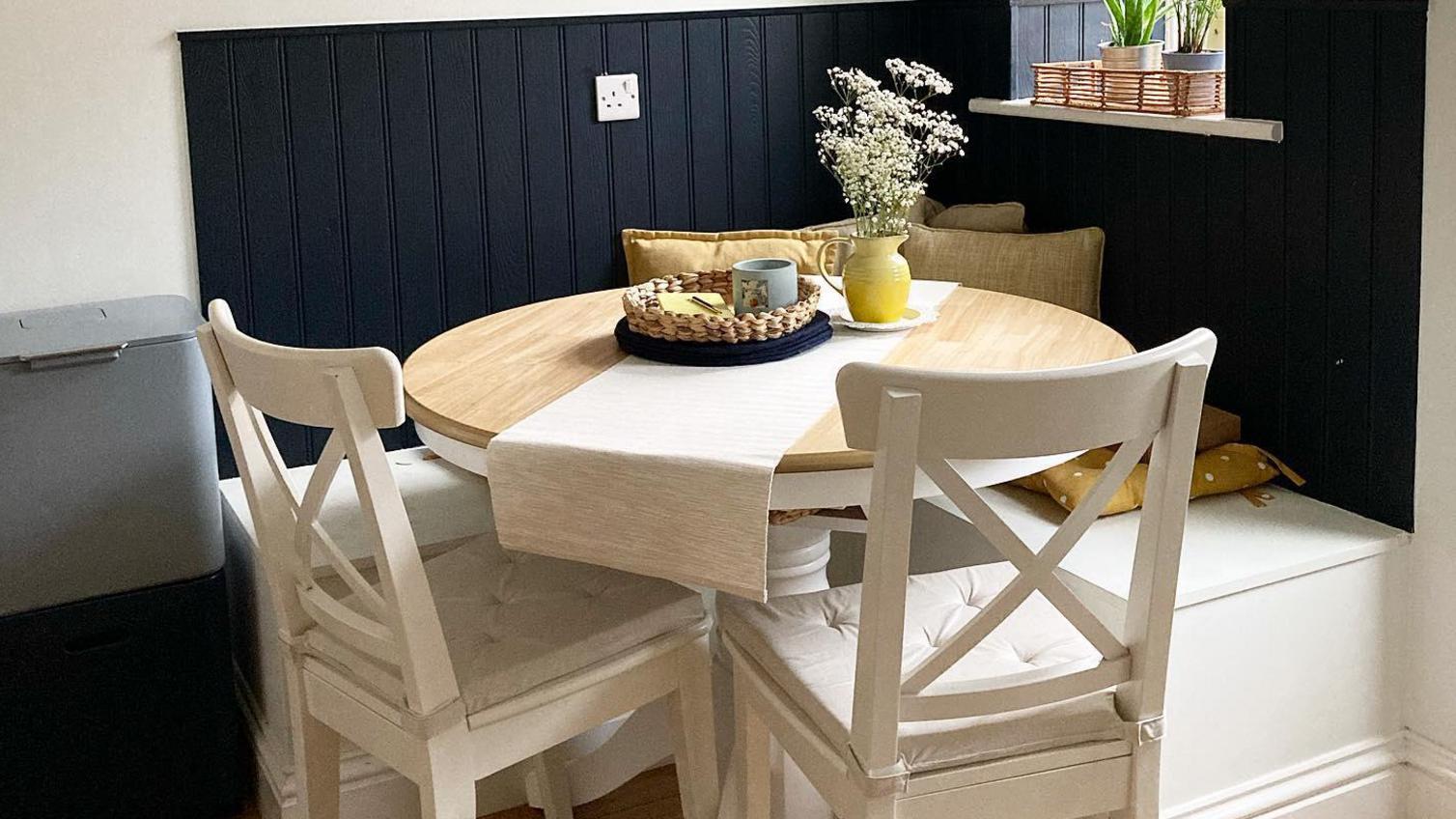 Round dining room table design with a light oak top, white farmhouse chairs, and a custom bench with navy wall panelling.