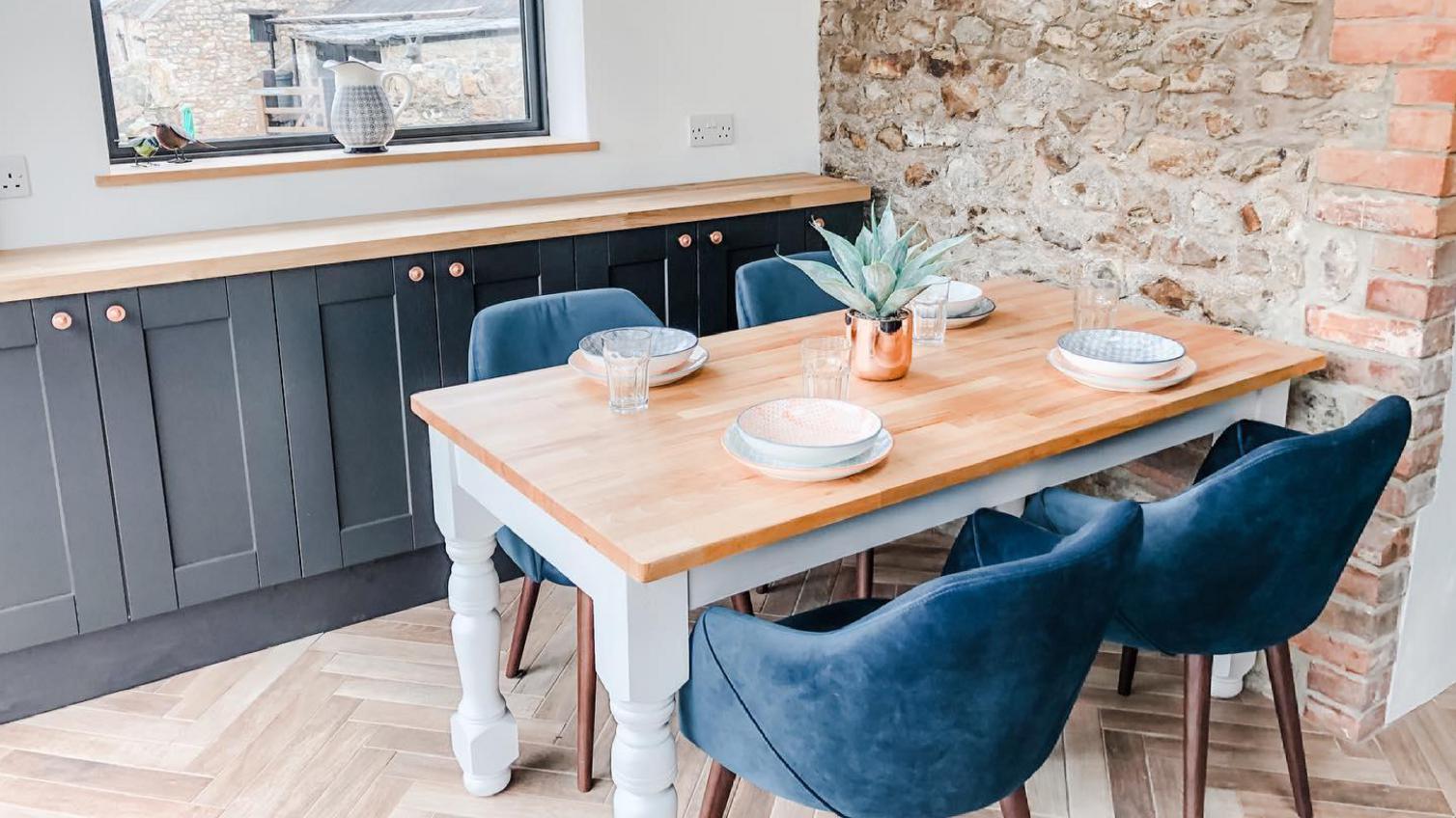Farmhouse dining room idea with an oak table, blue velvet chairs, exposed brick wall, and navy shaker base cupboards.
