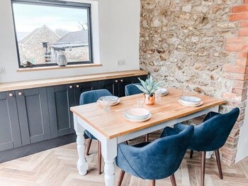 Farmhouse dining room idea with an oak table, blue velvet chairs, exposed brick wall, and navy shaker base cupboards.