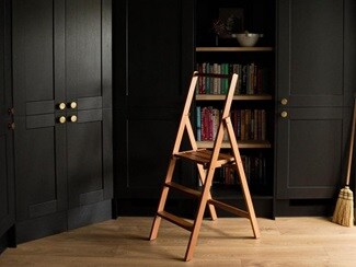 Black dining room idea with built-in tower cupboards, gold knob handles, a custom bookshelf, oak floors, and an oak ladder.