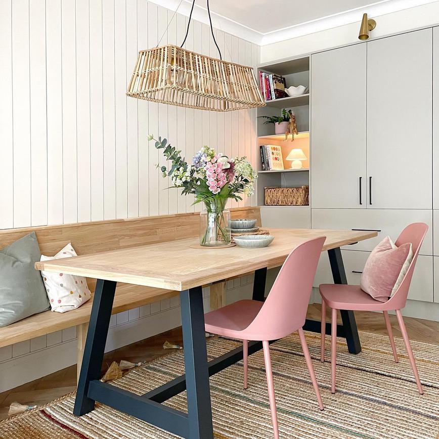 Scandi dining room idea with light grey slab doors, black handles, a custom oak bench, an oak table and pink chairs.