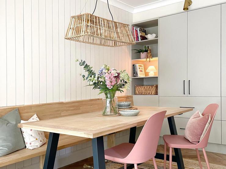 Scandi dining room idea with light grey slab doors, black handles, a custom oak bench, an oak table and pink chairs.