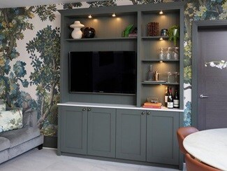 A green sideboard complete with lighting and a television, in a room decorated with floral wallpaper