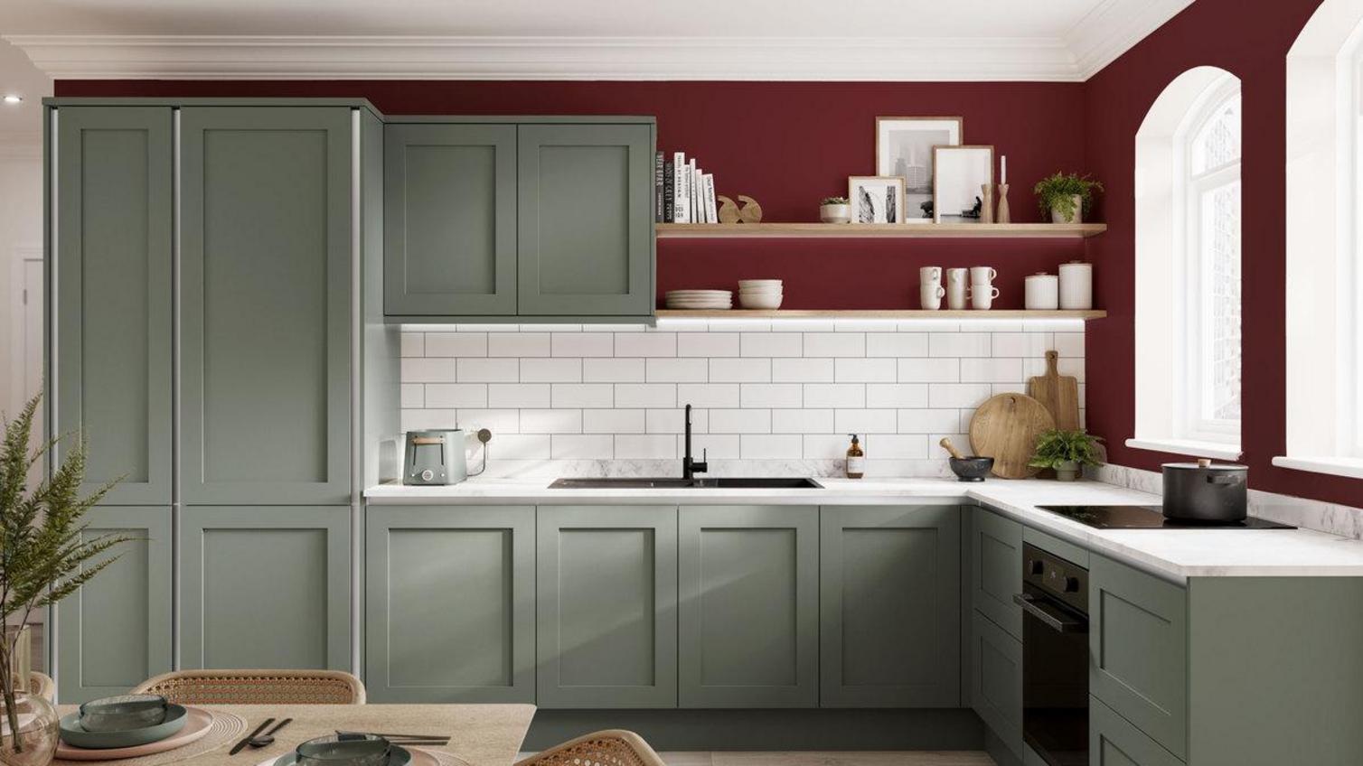 Simple red kitchen idea with a garnet-red feature wall. Includes sage-green shaker units, white worktops, and timber floors.