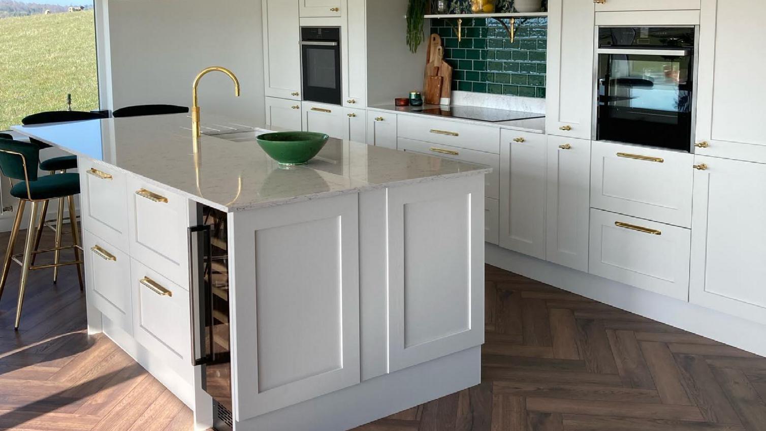 Classic shaker kitchen makeover featuring dove-grey doors, white worktops, aged-brass handles, and herringbone flooring.