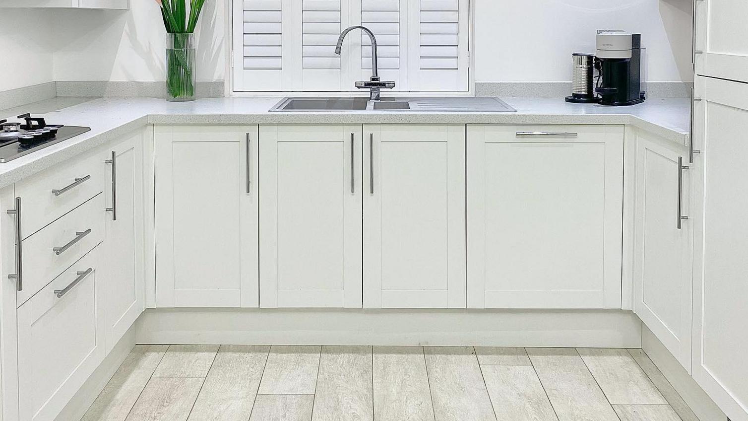 A small shaker kitchen in white, from the Allendale range, with a grey worktop and wood effect flooring.