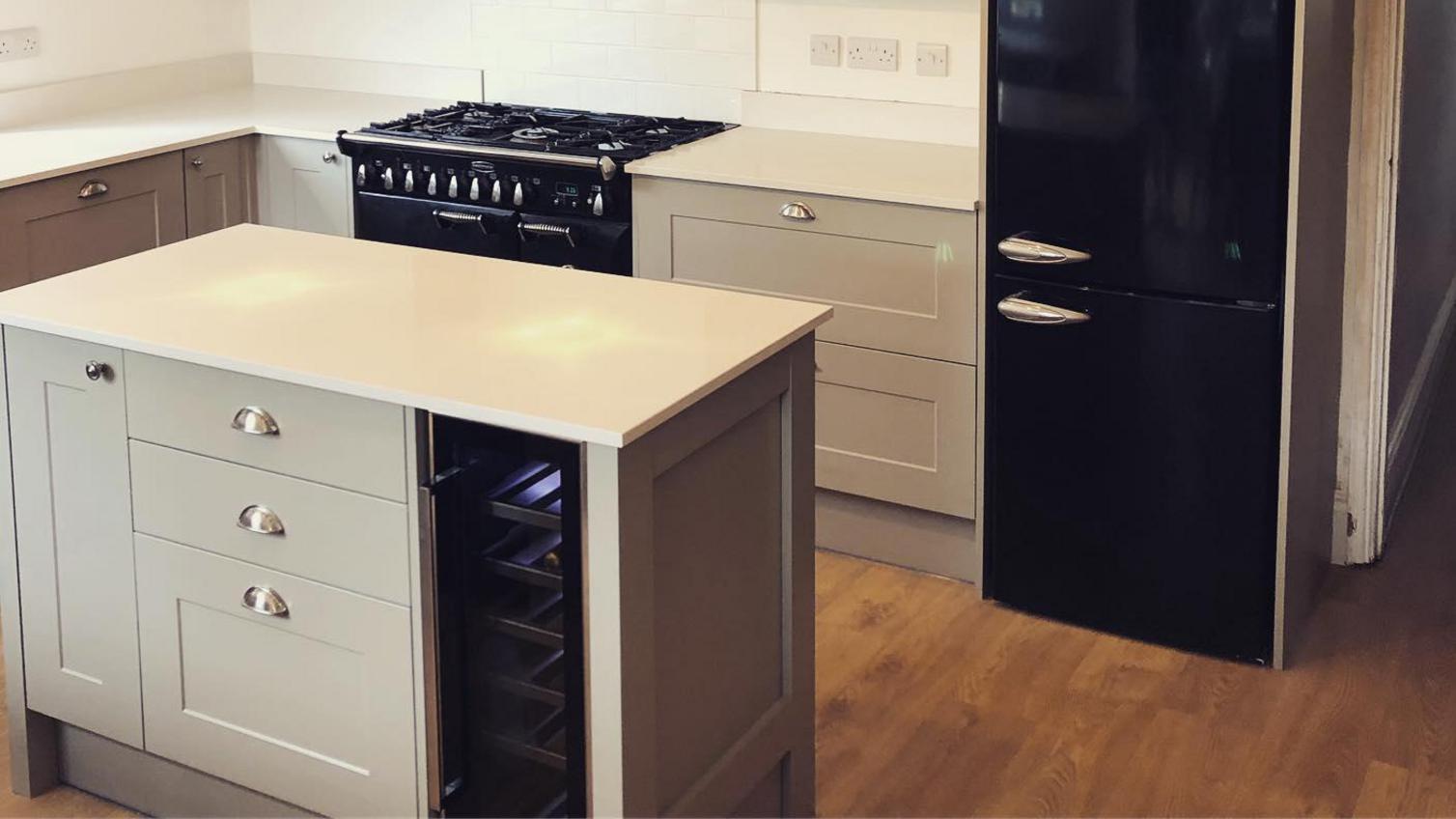 Small shaker kitchen from the Chelford pebble range. Features a small kitchen island with a black wine fridge.