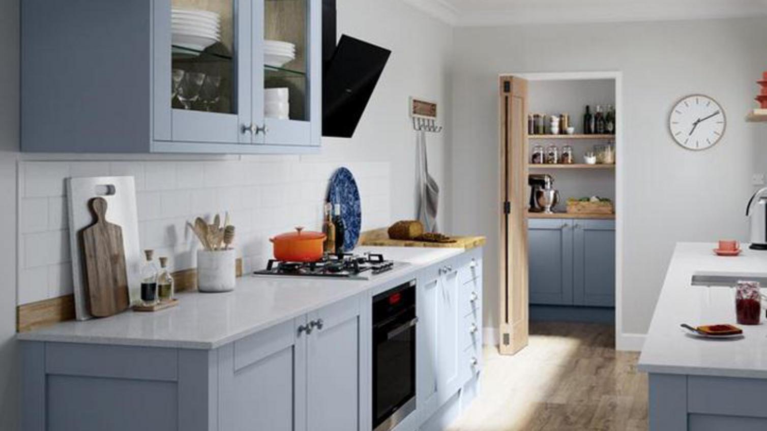 Small shaker kitchen in a galley layout, finished with a blue colour. Includes light worktop and glass wall cabinets.