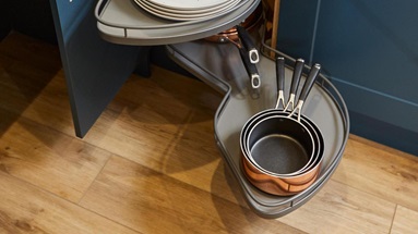Pull-out corner storage in a marine blue, small shaker kitchen. The storage has space for plates and saucepans.