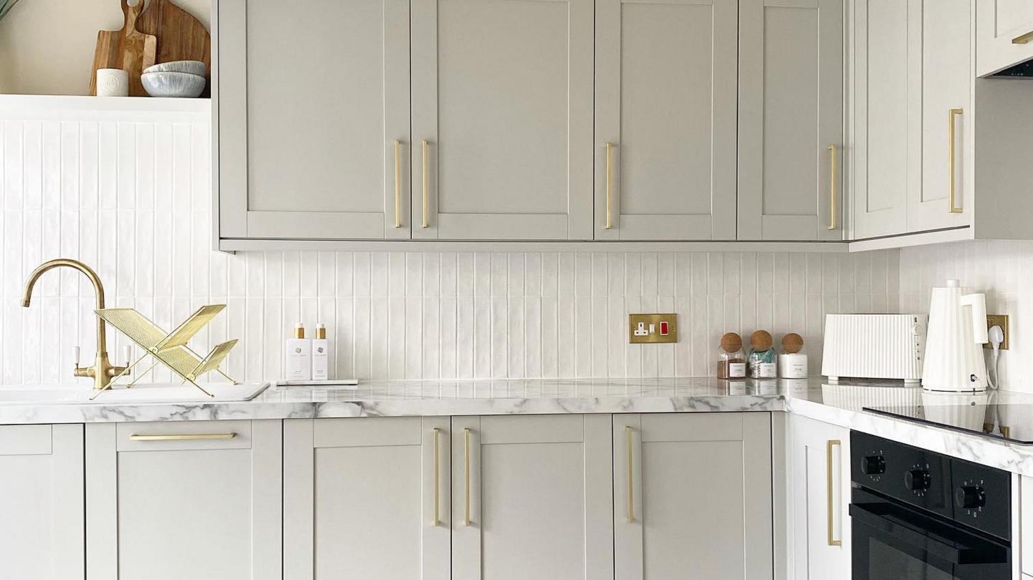 A bright white shaker kitchen accented in gold, with a backing of clean white wooden wall panelling
