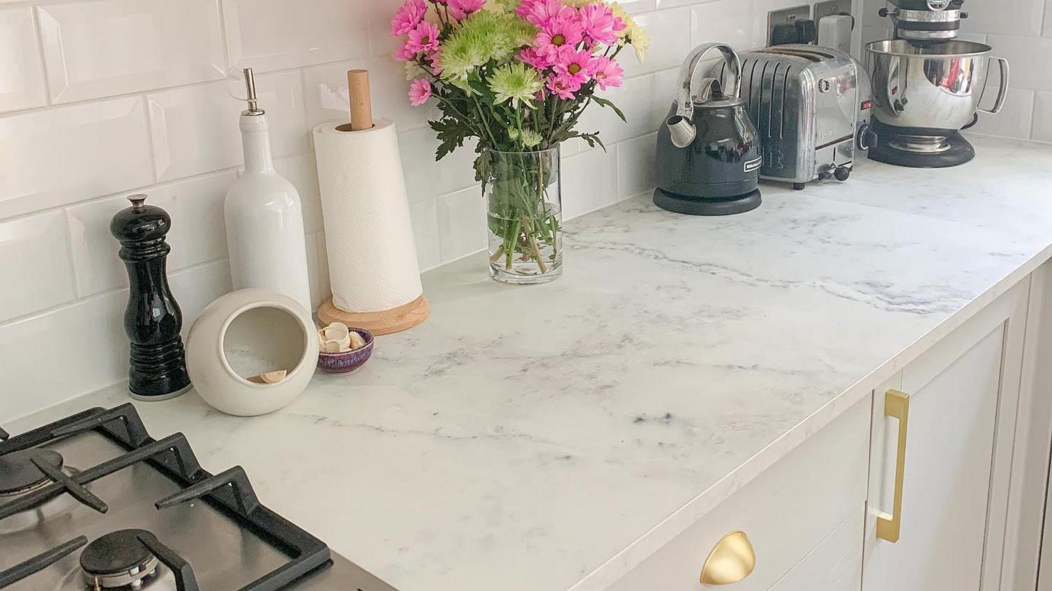 A white, marble-effect laminate worktop in a bright and gold kitchen