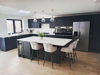 Shaker kitchen island idea with navy units, white worktops. wood flooring, and a black wine cooler.