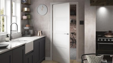 A white fire door inside a dark blue kitchen with pale wooden flooring
