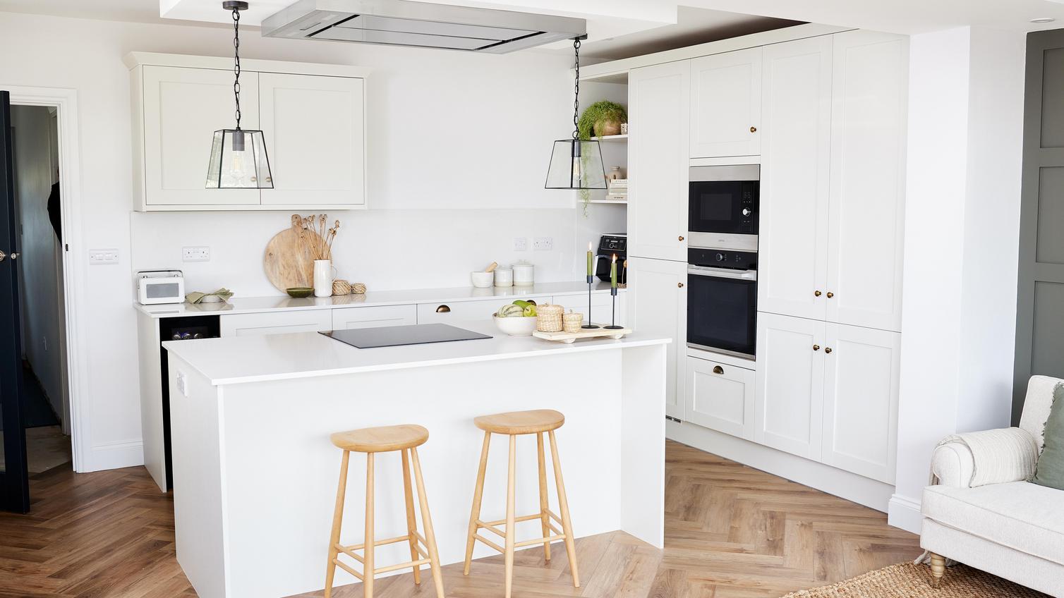 A white Halesworth kitchen from Howdens, in a island layout and with light wooden furniture and accessories