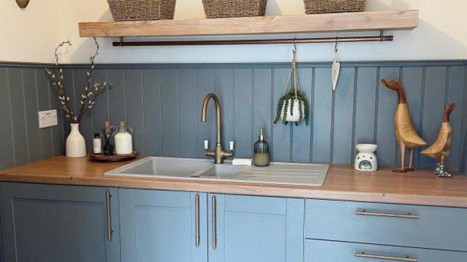 A blue shaker utility room with a laminate worktop, timber shelving, and wood panelling.