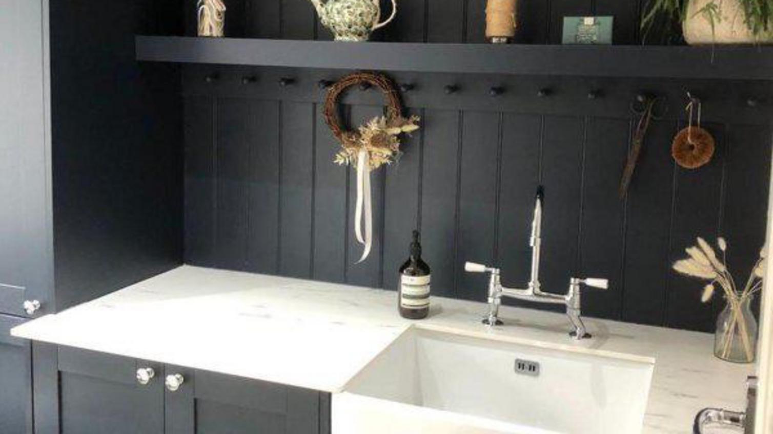 A bold, black utility room with matching shelving and wood panelling, and a white marble worktop and deep belfast sink.
