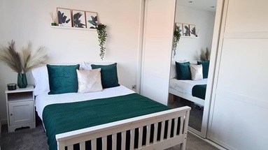 A white and green modern bedroom space, with slliding mirrored wardrobe doors