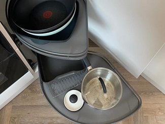 Grey corner pull-out accessory with two shelves. Chevron flooring and white marble worktop.