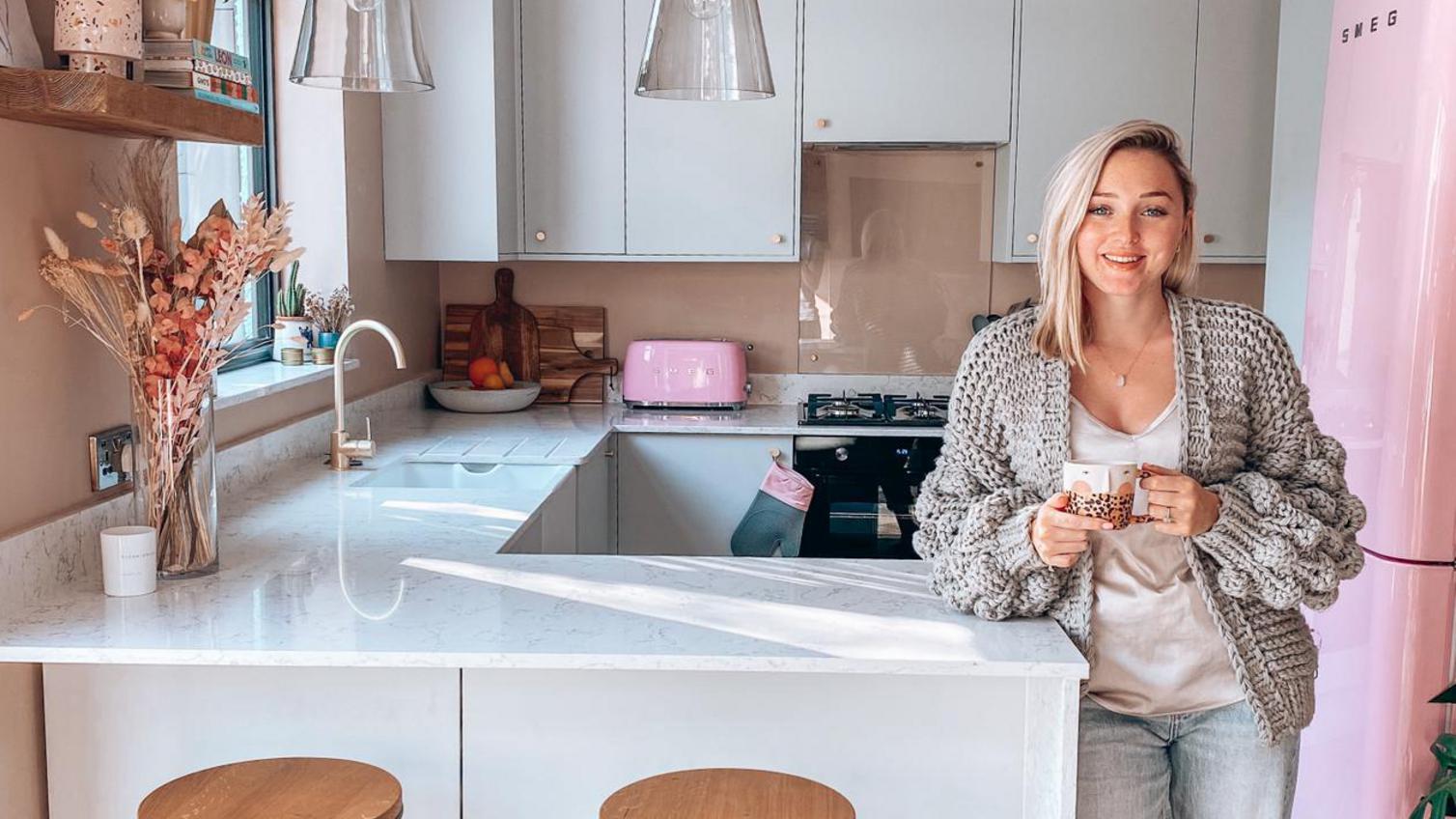 Woman in a grey slab kitchen with a peninsular design, standing next to a breakfast bar with a white marble quartz worktop.