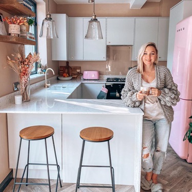 Woman in a grey slab kitchen with a peninsular design, standing next to a breakfast bar with a white marble quartz worktop.