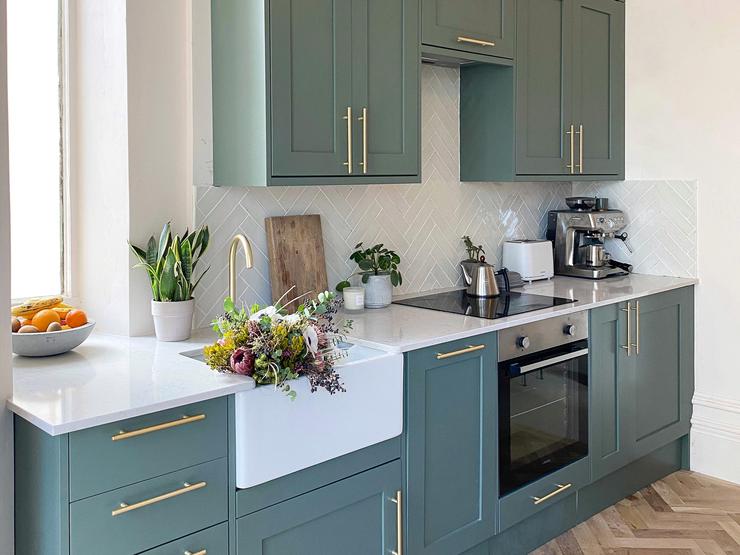 Paintable single wall kitchen idea with teal shaker cupboards, brass bar handles, a white worktop and a white belfast sink.