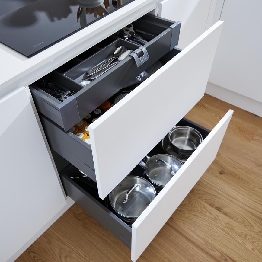 A compact white kitchen with two pan drawers and cutlery tray fitted beneath a black induction hob.