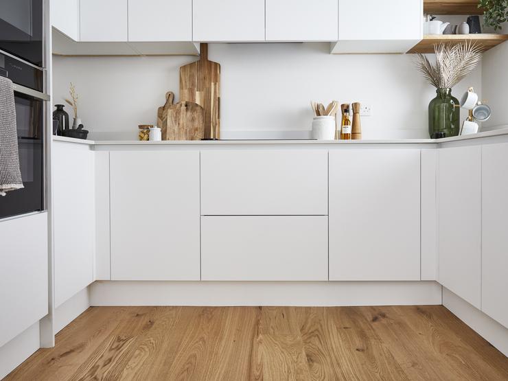 A white handleless kitchen in a u-shaped layout. Includes white trims, wooden flooring, and quartz worktops.