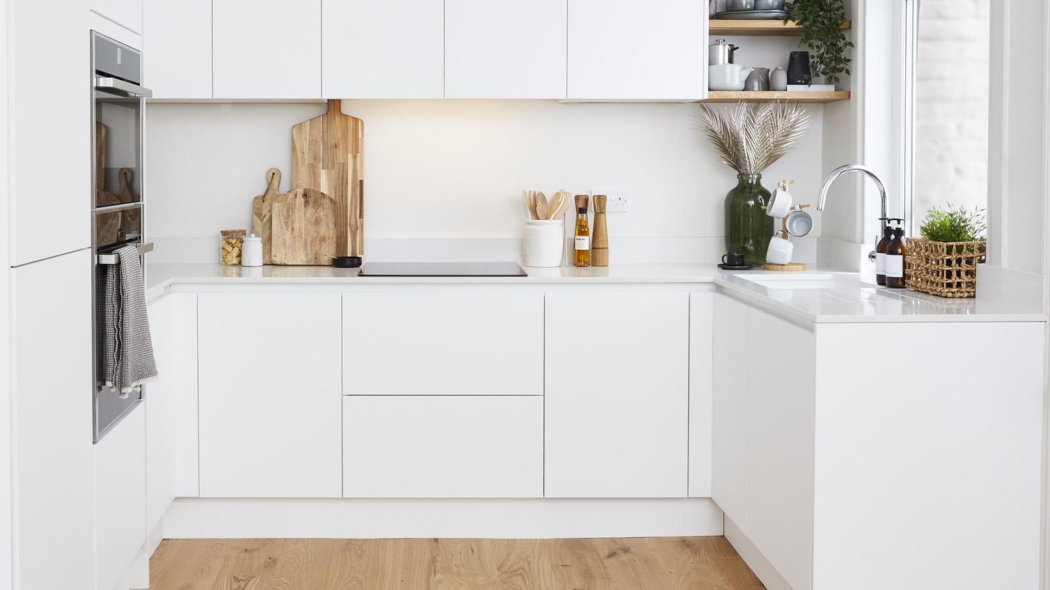 A u-shaped white handleless  kitchen with super matt cupboard doors. Includes a built-in double oven and an induction hob.