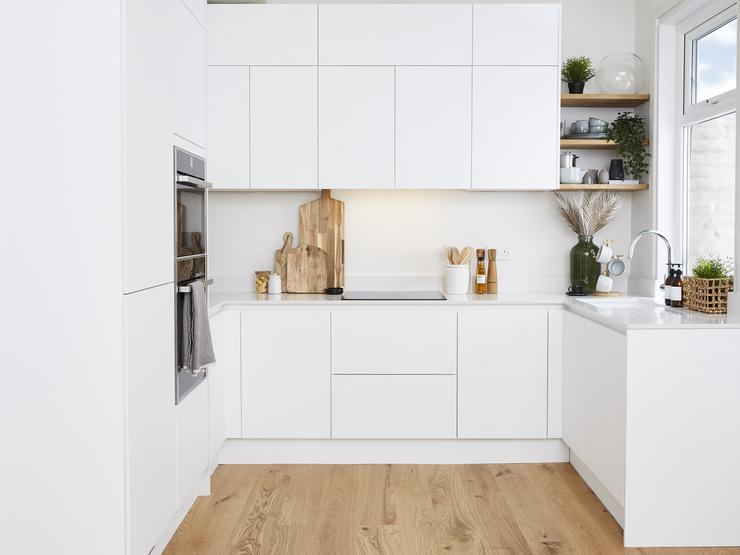 A u-shaped white handleless  kitchen with super matt cupboard doors. Includes a built-in double oven and an induction hob.