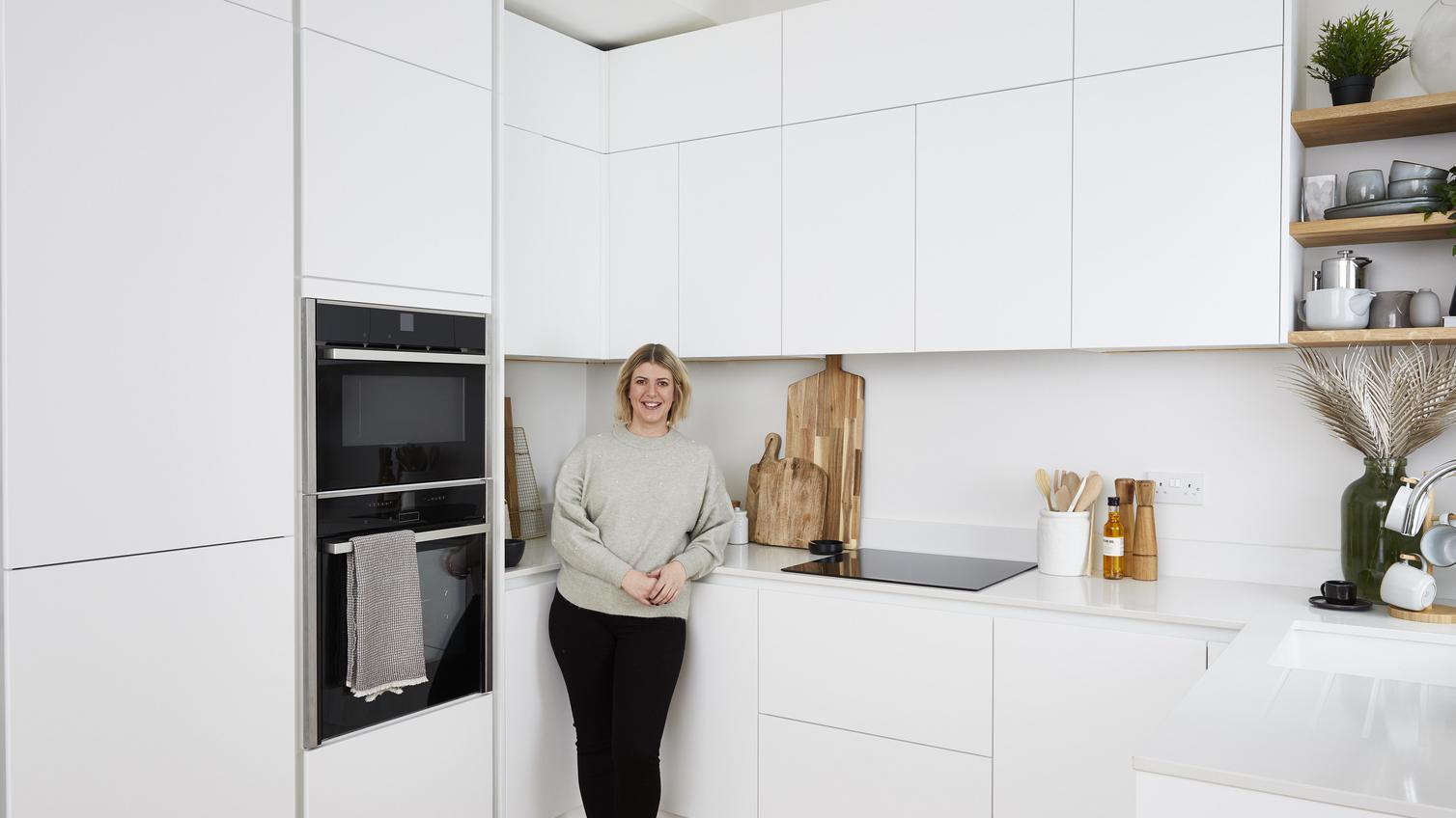 Women standing in a u-shaped white kitchen. Has a modern handleless design and includes white quartz worktops.