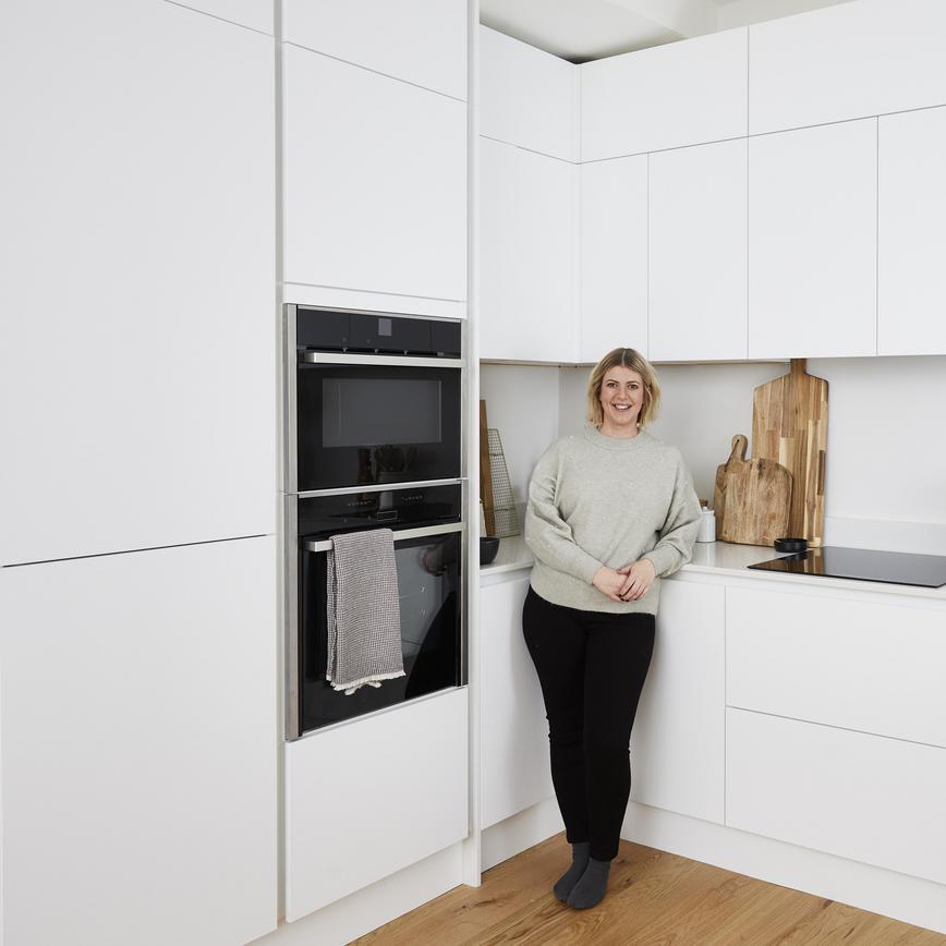Women standing in a u-shaped white kitchen. Has a modern handleless design and includes white quartz worktops.