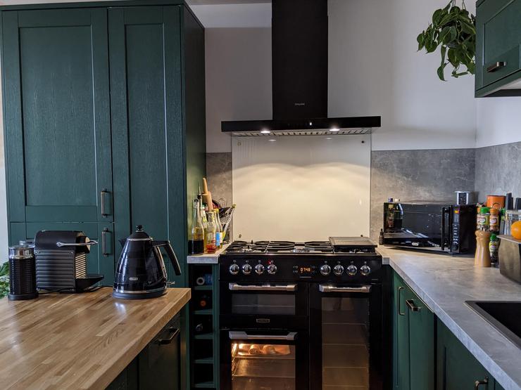 Dark green kitchen design in an island layout, with oak-effect flooring and worktops, and grey concrete effect worktops.