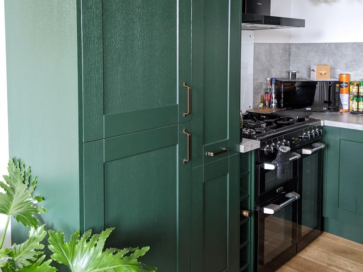 Dark green kitchen with shaker doors, a full-length larder unit, oak flooring, black hob, extractor fan and brass handles.