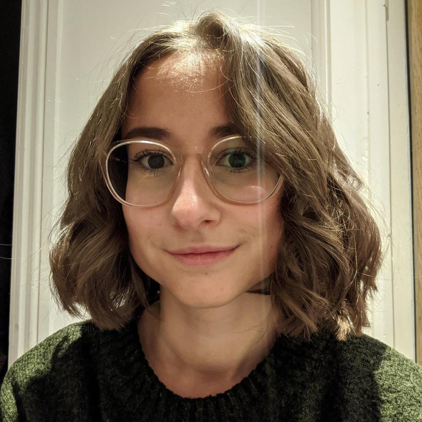 Image of Mathilde smiling, with short brown hair, a dark green jumper and glasses.