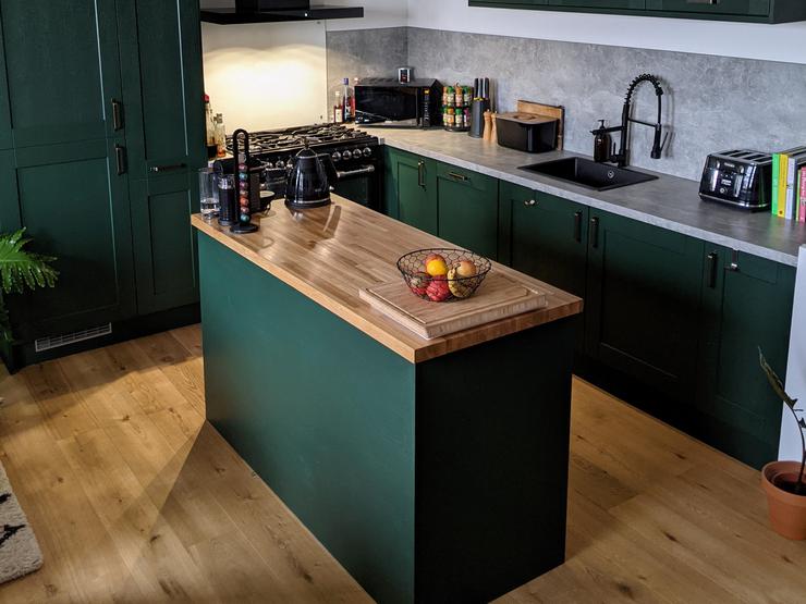 Green shaker kitchen with an island layout, with oak worktops and flooring, and a grey concrete-effect backboard.