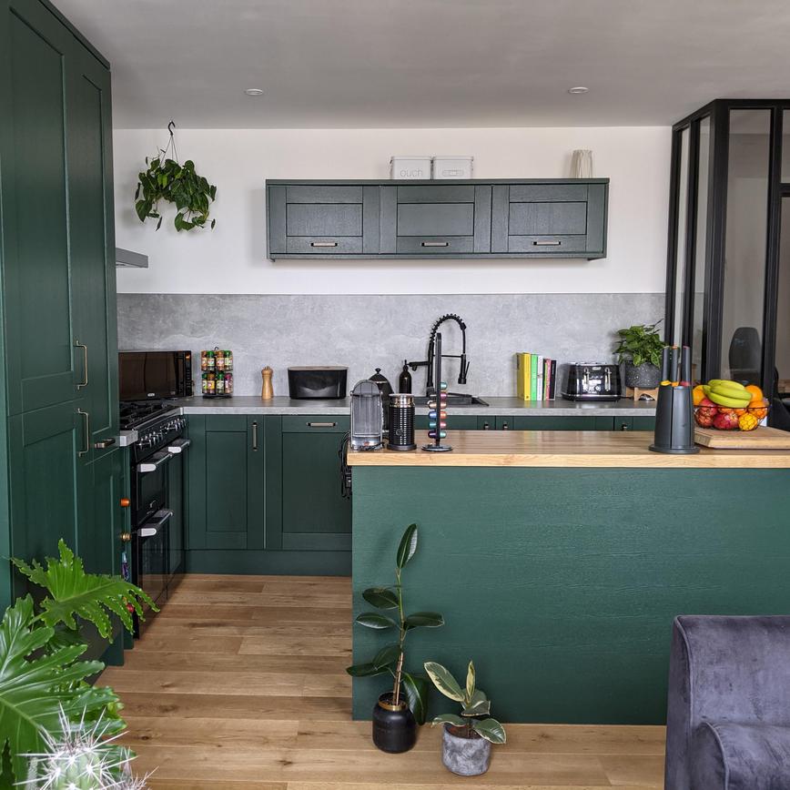 Green shaker kitchen idea with island layout, matching oak floors and worktops, with concrete-effect surfaces and backboard.