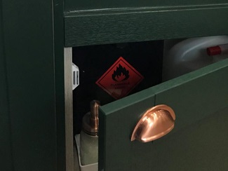 Close-up of door hinge showing soft-close setting, with dark green shaker door, copper cup handles and white Belfast sink.