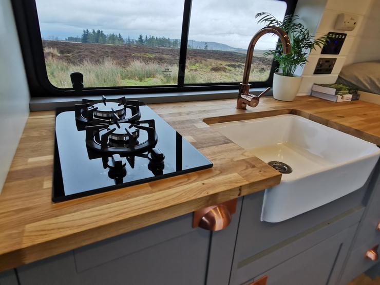 a blue shaker kitchen in a campervan conversion with a domino gas hob and ceramic sink.