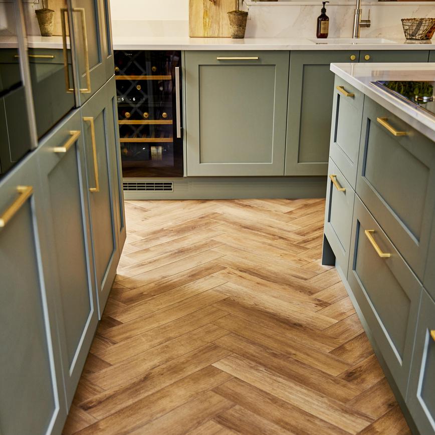 Sage green shaker kitchen design with antique wood chevron flooring, brass bar handles, and a wine fridge.