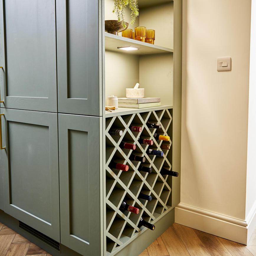Sage green shaker kitchen design with built in cupboards on the side of unit, with accessories and a custom wine rack.